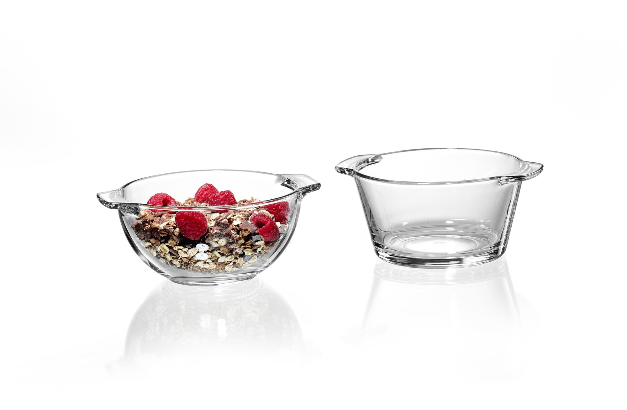 Runde Glas-Schalen, eine mit Müsli und Himbeeren, eine leer