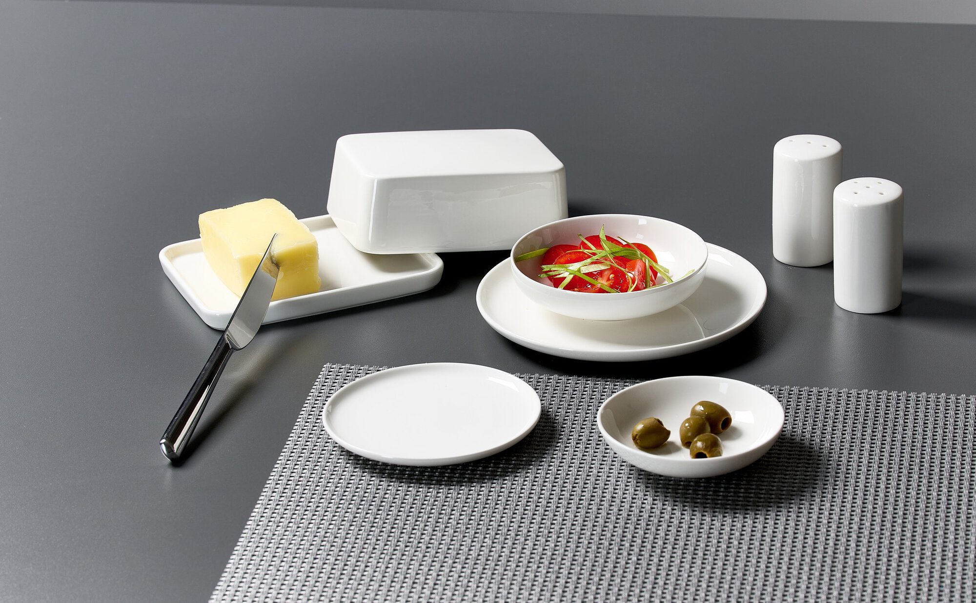 Weißes Tafelservice mit Butter, Tomaten und Oliven auf graue