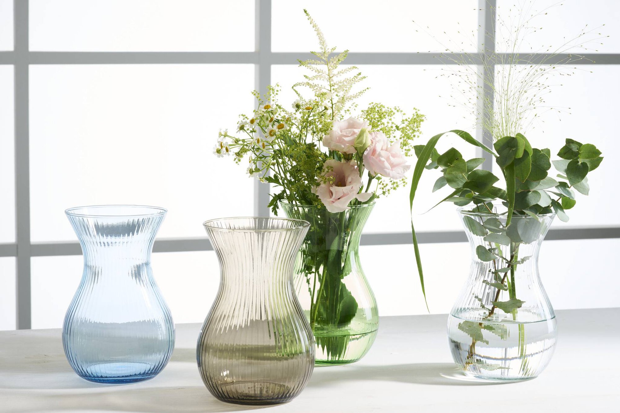 Vasen aus farbigem Glas mit Blumen und grünem Laub