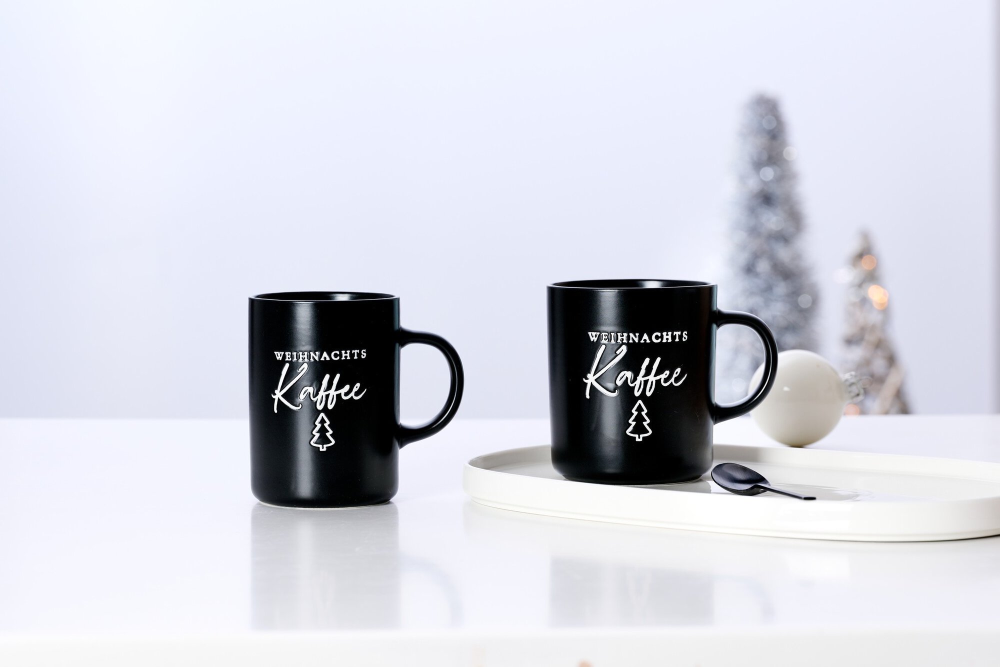 Schwarze Kaffeetassen mit Weihnachtsmotiv auf weißem Tisch
