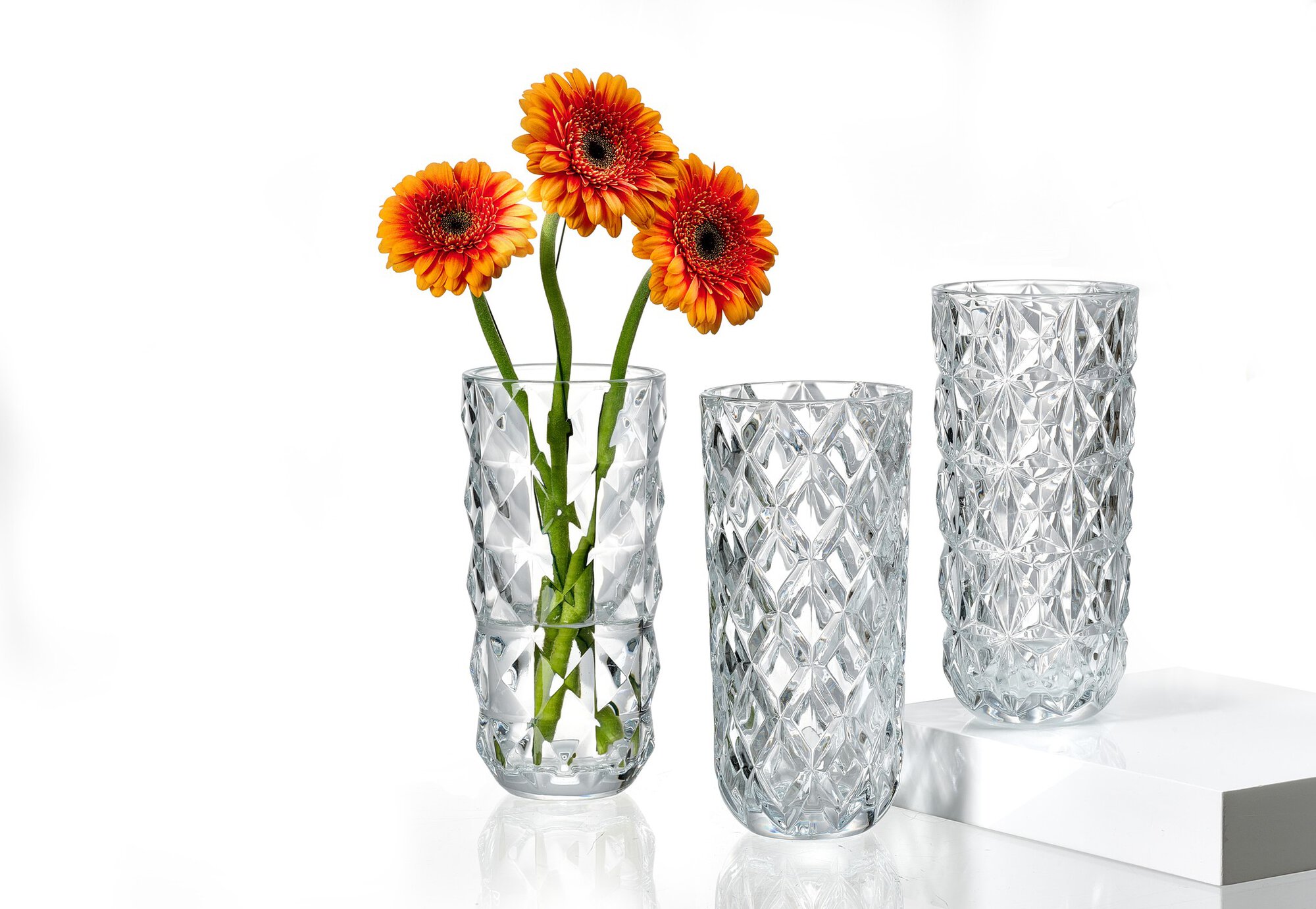 Drei Kristallglasvasen, eine mit orangen Blumen gefüllt