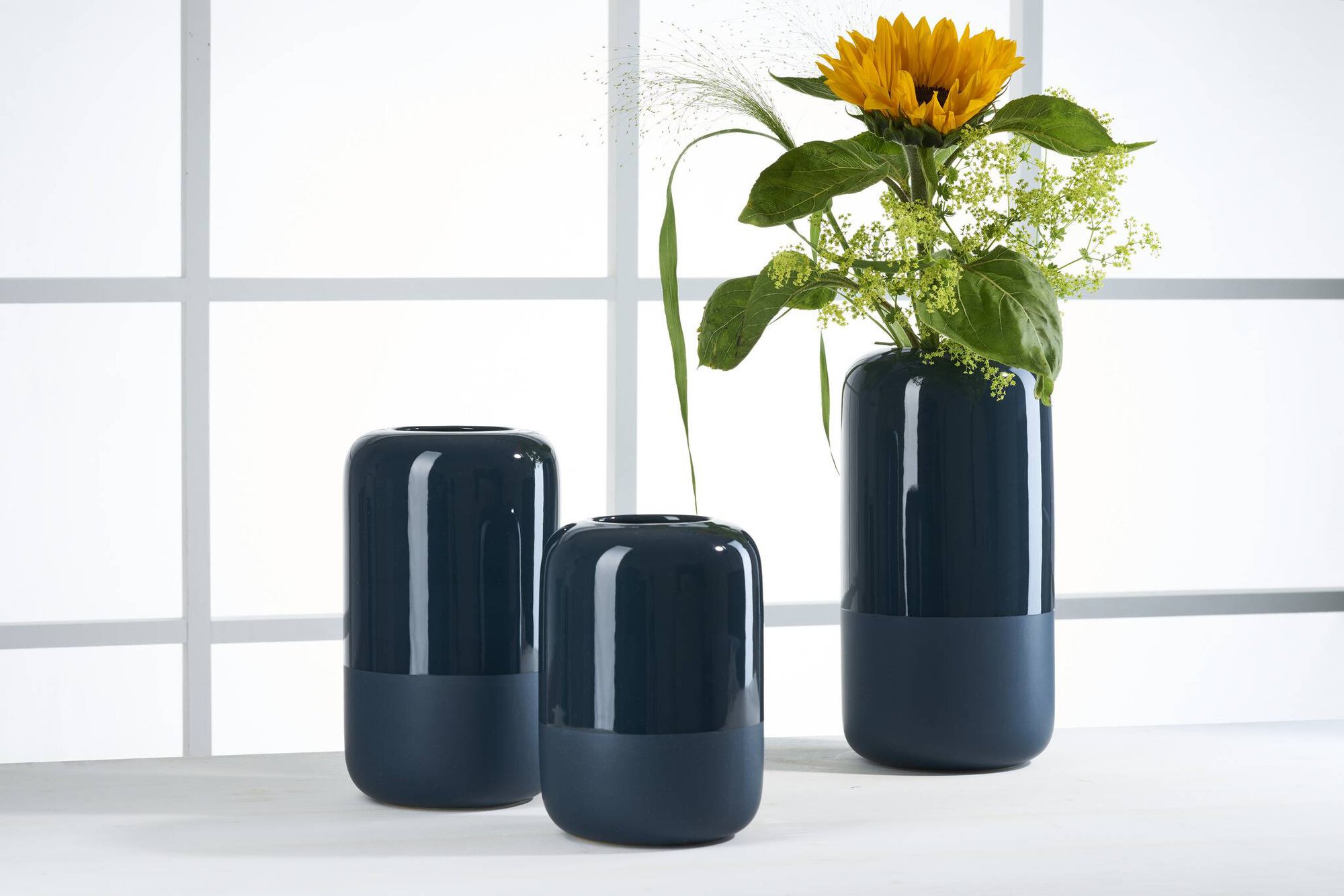 Drei blaue Vasen, eine mit gelber Sonnenblume und grünen Blä