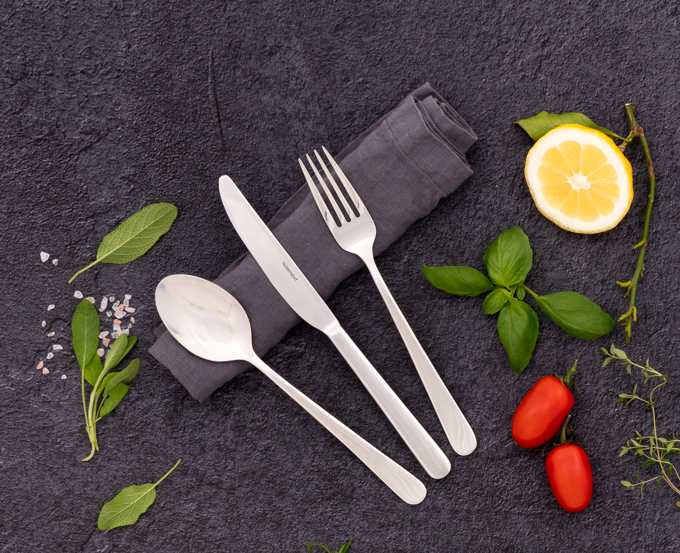 Edelstahlbesteck mit Messer, Gabel, Löffel und Kräutern