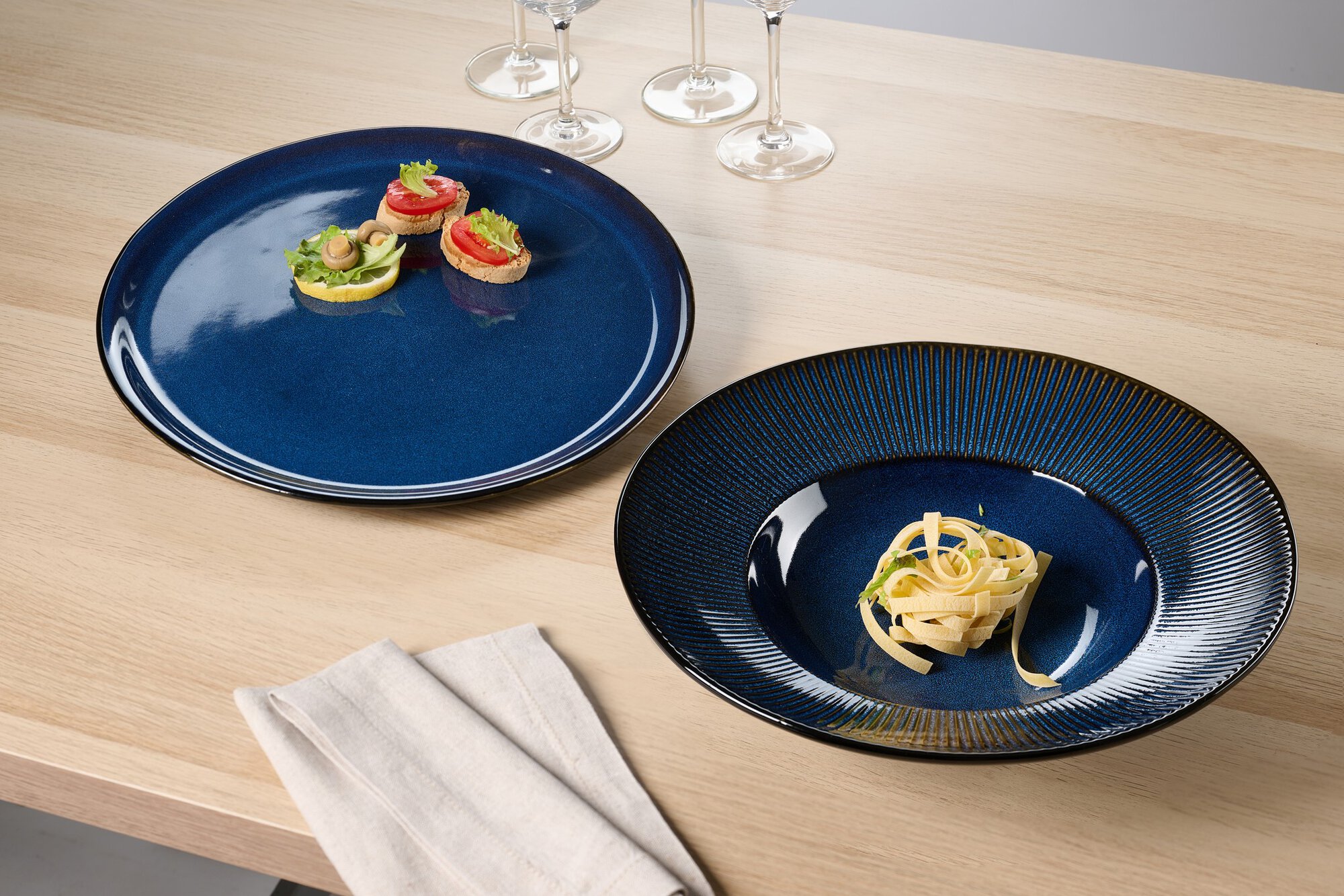 Blauer Teller mit Pasta und kleiner Snack auf hellem Holztis