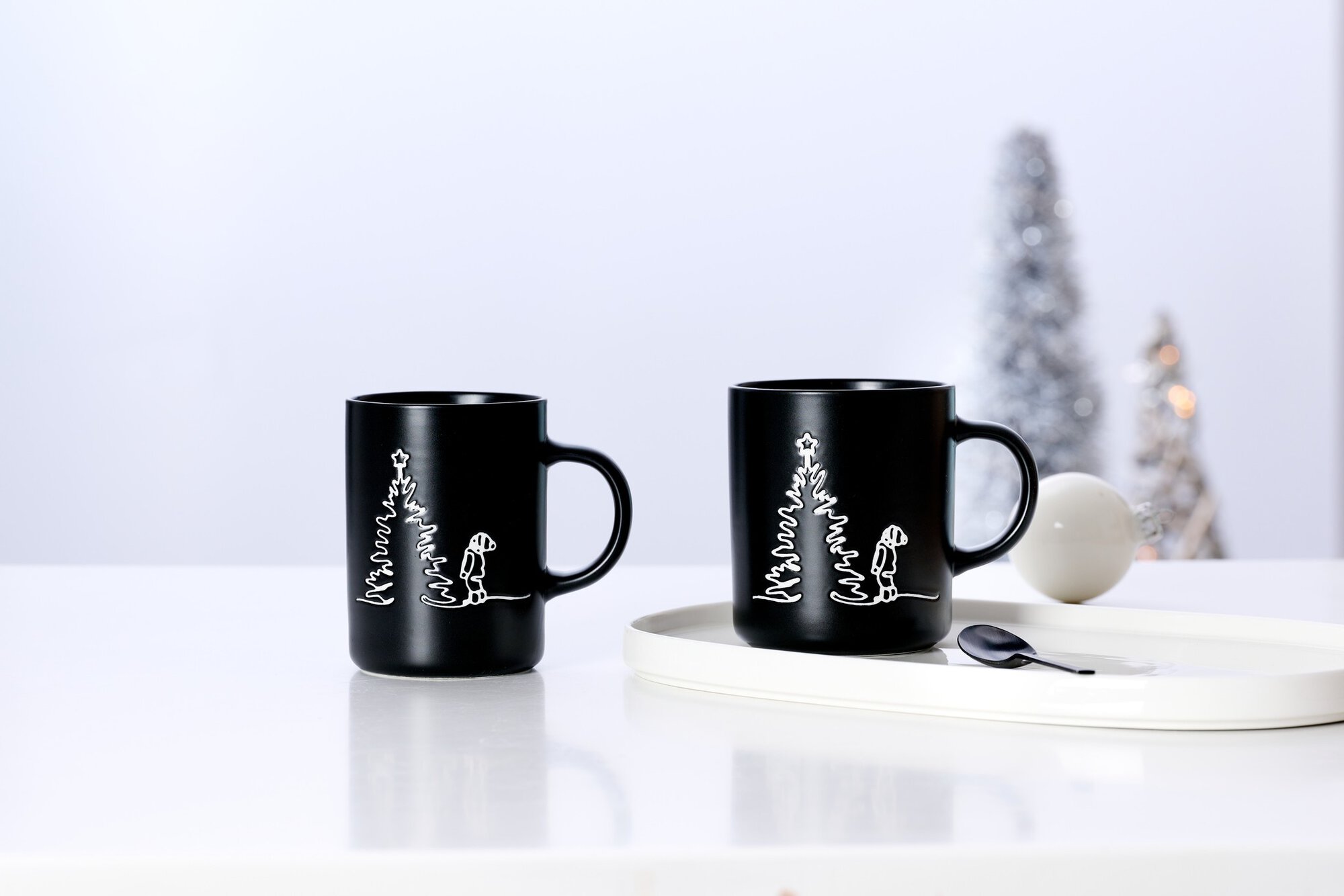 Zwei schwarze Tassen mit Weihnachtsbaum und Hund auf weißem