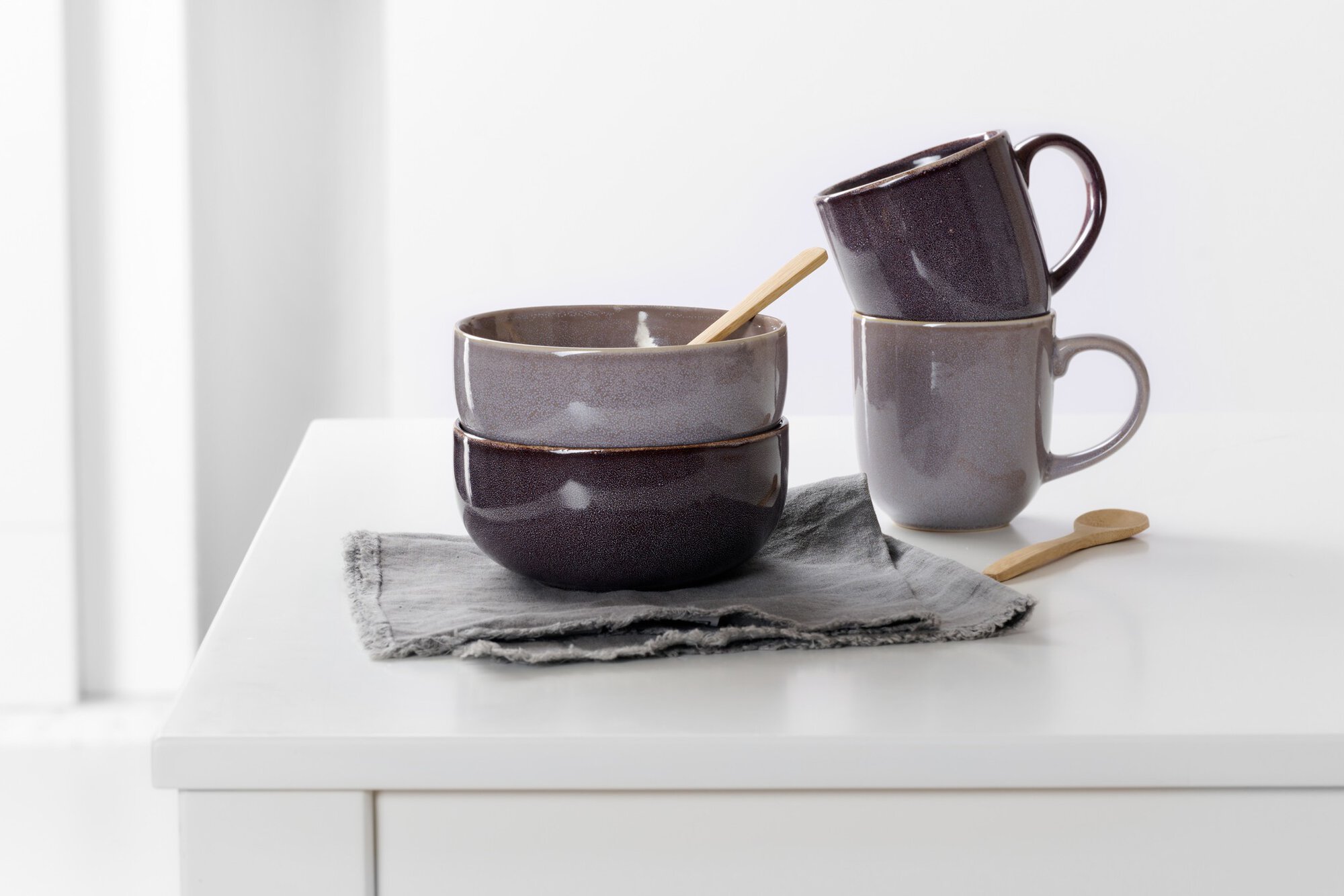 Zwei Keramikschalen und zwei Tassen mit Holzlöffeln auf grau