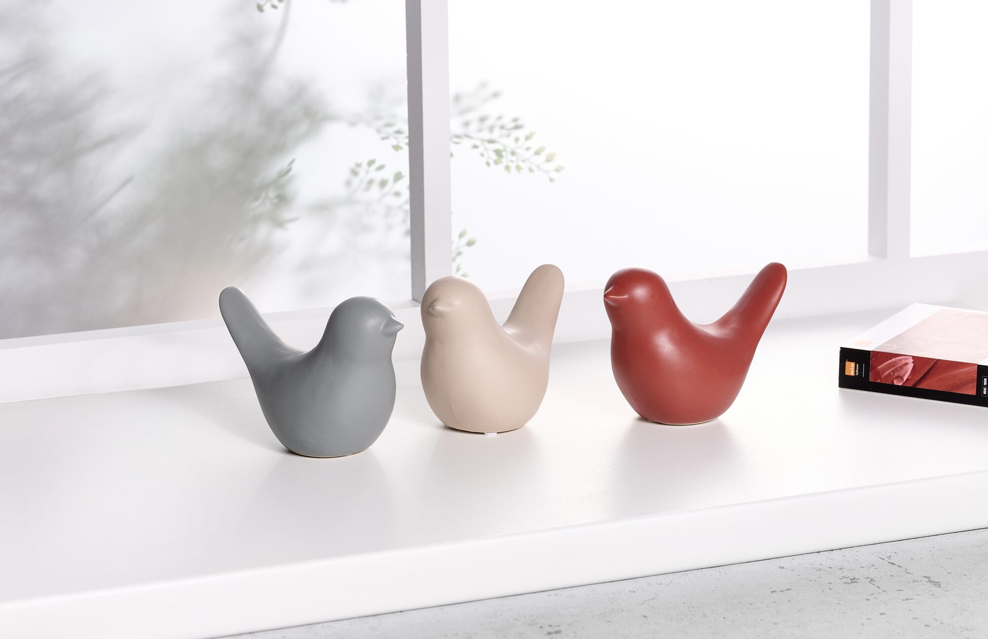 Keramik-Vögel in Grau, Beige und Rot als Deko auf weißem Fen