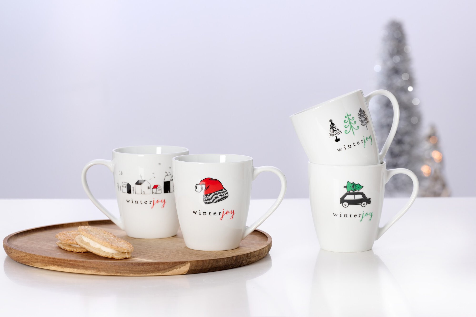 Vier Winter Joy Tassen mit Weihnachtsmotiven auf weißem Tisc