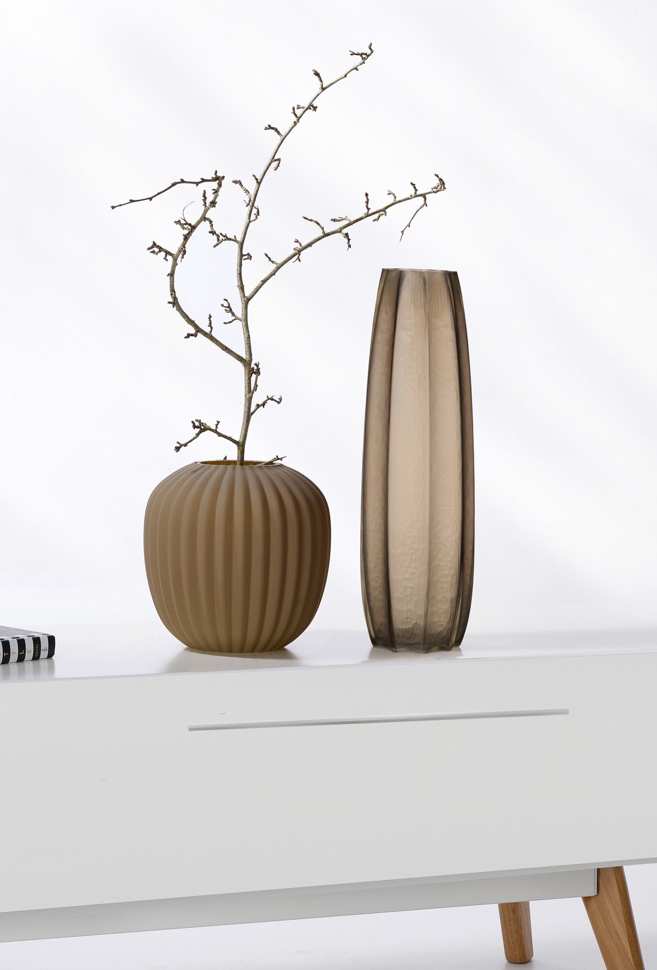 Braune Glasvase und Keramikvase mit Zweig auf weißem Möbel