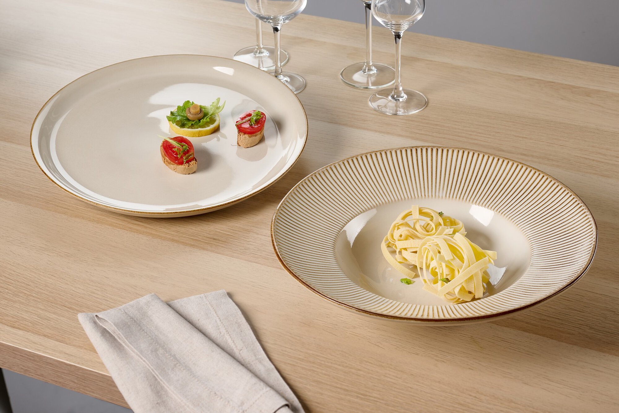 Zwei elegante Teller mit Pasta und Canapés auf Holztisch