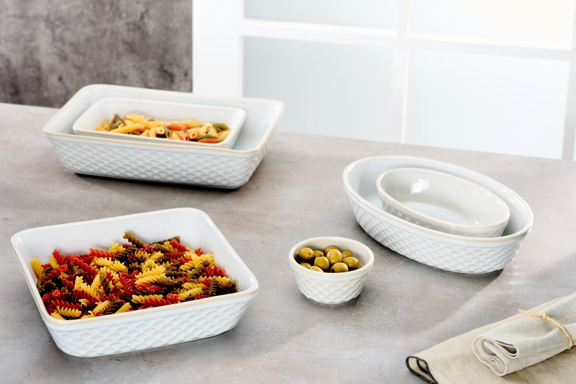Verschiedene weiße Keramikschalen mit bunter Pasta und Olive