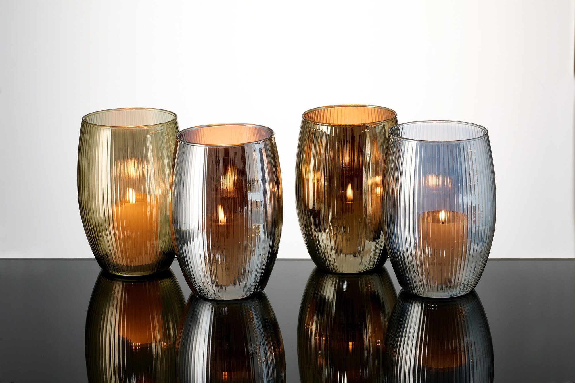 Vier Kerzenhalter aus geriffeltem Glas mit brennenden Kerzen