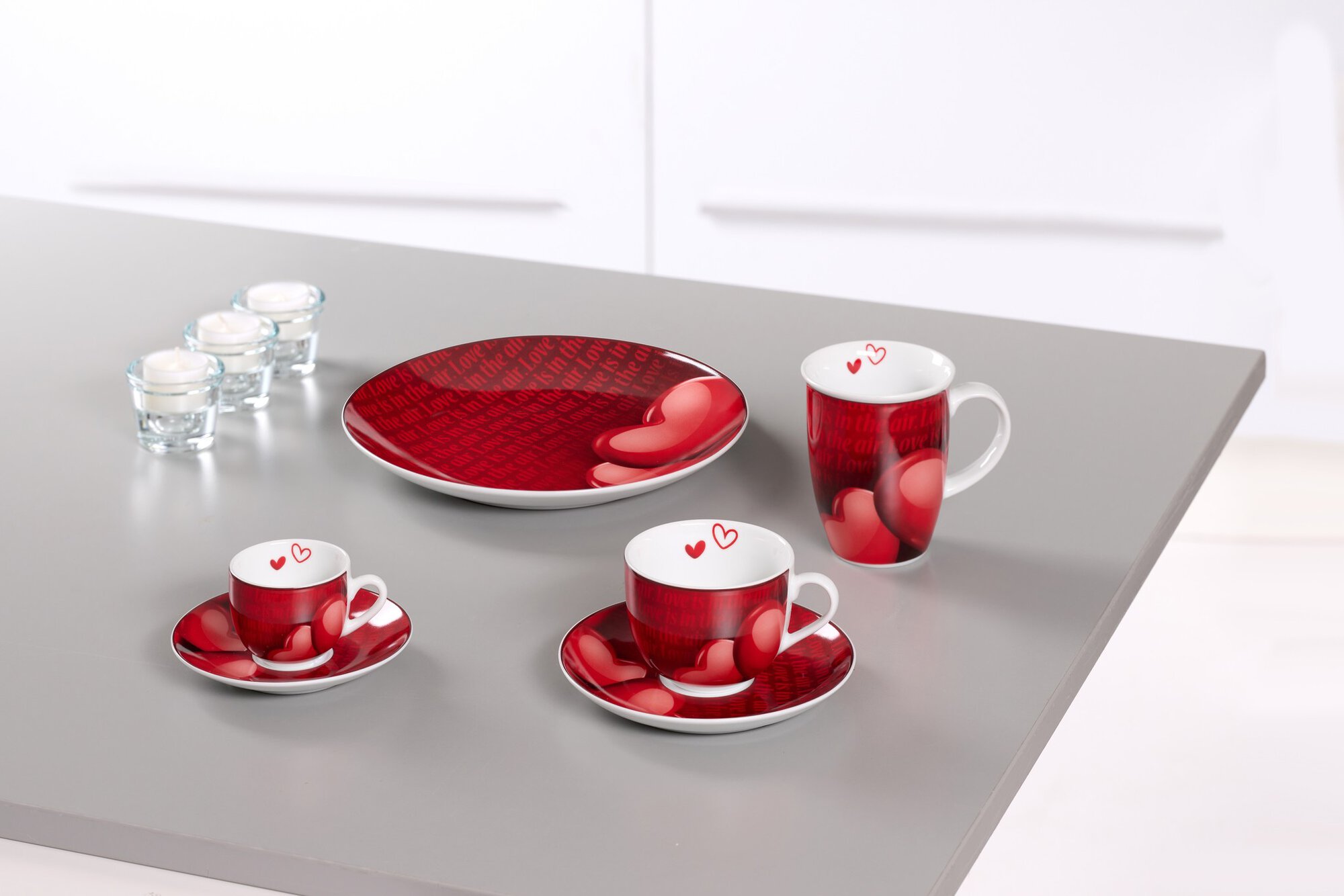 Kaffeetassen und Teller mit roten Herzen auf grauem Tisch