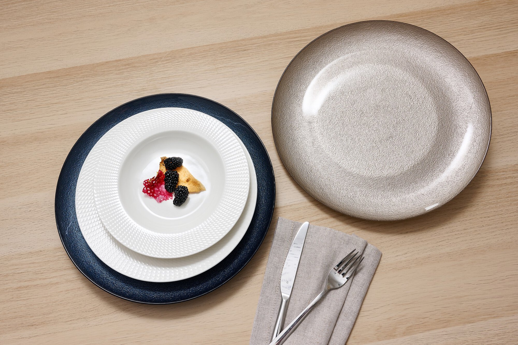 Drei Teller mit Dessert und Besteck auf hellem Holztisch
