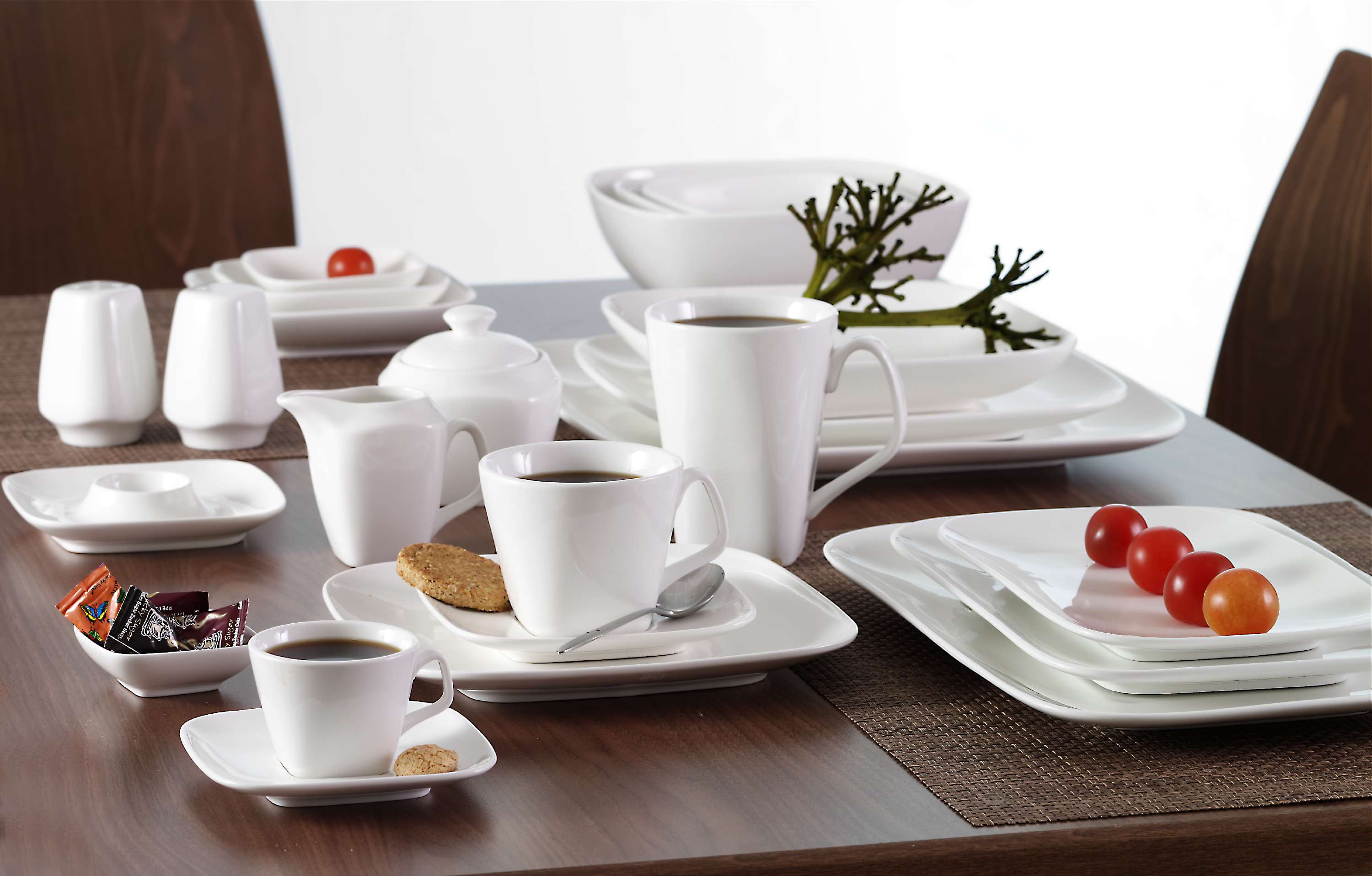 Weißes Geschirr mit Kaffee, Keks und Tomaten auf Holztisch
